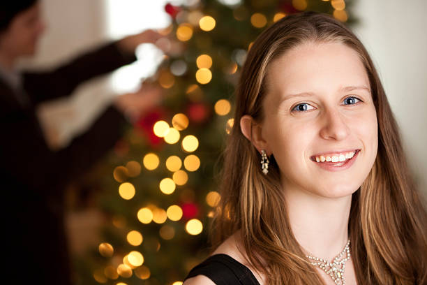 Classy Young Woman At Home during Christmas While Husband Decorates Tree.See more from this series: