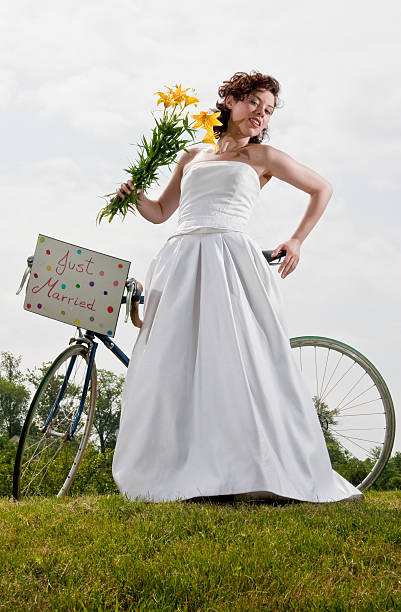 A woman showcases a unique dress crafted from newspaper, standing on a wooden porch surrounded by lush greenery. She poses confidently, exemplifying innovative fashion design.