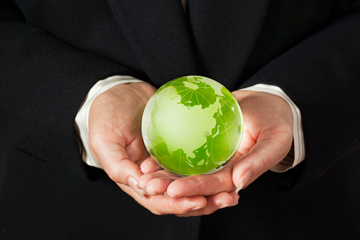 The hands of a corporate business executive in business suit holding a green globe, promoting the business ethics of green global environmental responsibility and consciousness.