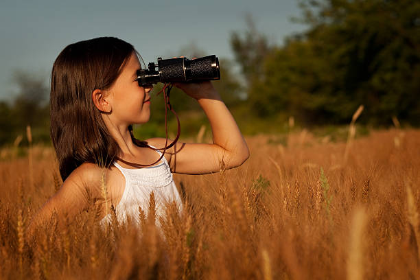 istock Cute young girl using binoculars in Field of Brown-stalked Grain 182844016