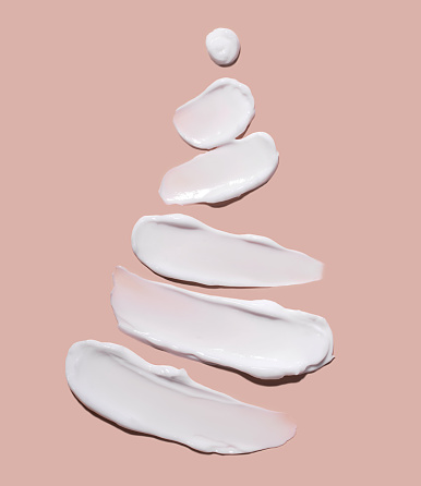 The concept of a Christmas tree in the form of cosmetic strokes on a pink background. Cream for skin care.