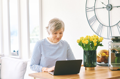 Indoor portrait of happy middle age woman working at home with laptop
