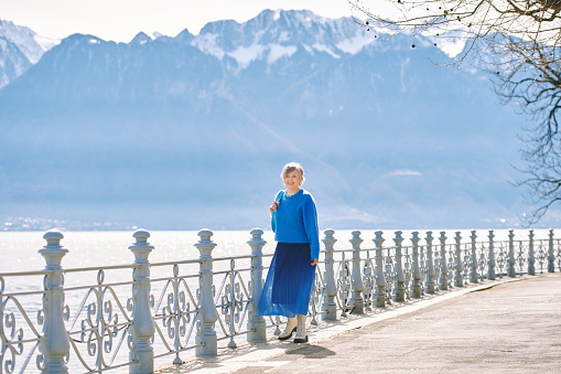 Outdoor fashion portrait of happy mature woman walking by the lake, wearing blue  pullover and skirt