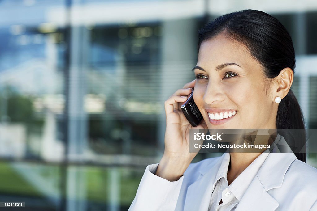 Asian Businesswoman on a Cellphone Beautiful Asian businesswoman smiles while talking on a mobile phone outside an office building. Horizontal shot. 30-39 Years Stock Photo