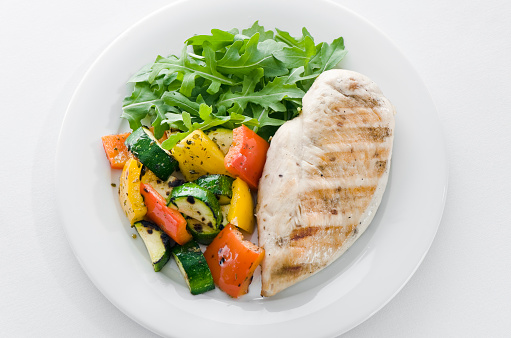 Grilled chicken and vegetables with arugula salad on a white background 