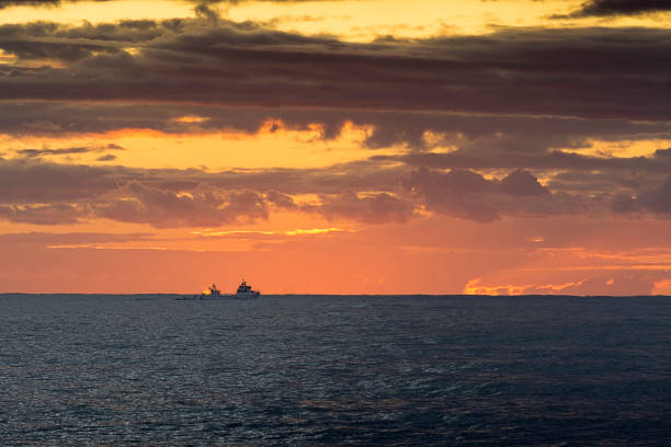 A commercial fishing boat navigates along the north coast of Portugal at sunset.