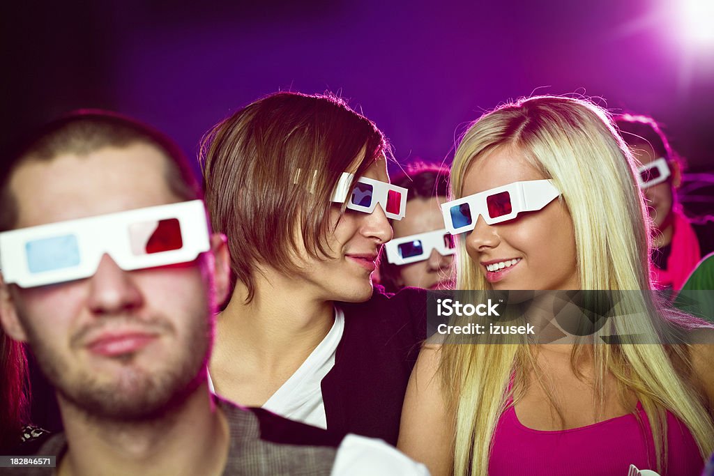 Young people in 3D move theater "Young adult people wearing 3D glasses, sitting in the cinema  and watching 3D move. Couple sitting in the middle smiling and looking at each other." 3-D Glasses Stock Photo
