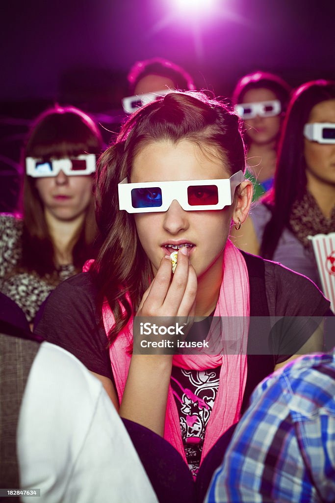 Young people in 3D move theater "Group of young adult people wearing 3D glasses, sitting in the cinema  and watching 3D move. Teenage girl sitting in front of eating popcorn." 3-D Glasses Stock Photo