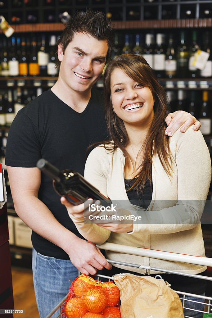 Coppia carina sorriso mentre si visualizza per vino in un supermercato - Foto stock royalty-free di Abbigliamento casual