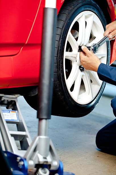 istock mechanic putting wheel on with jack 182848063
