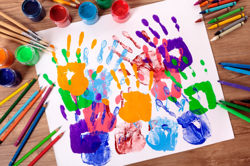 Painted handprints with art and craft equipment on a school table.  Alternative file of just the handprints shown below: