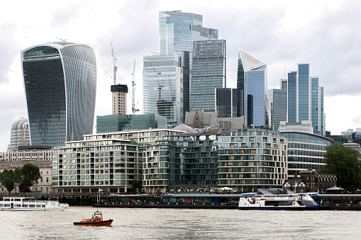 View of modern skyscrapers and buildings in London soaring above boats on the River Thames, cityscape features the unique walkie-talkie building - London, UK