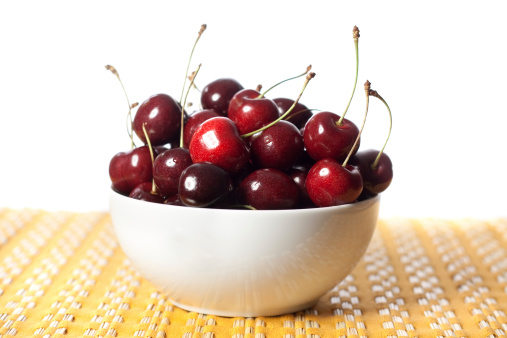 A bowl of delicious cherries on a yellow textured placemat