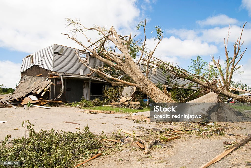 Wreckage of a neighborhood after a hurricane A fallen tree rests on a damaged house in the wake of a storm. Damaged Stock Photo