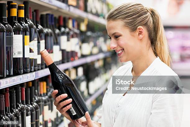 Woman Looking At Bottle Of Wine Stock Photo - Download Image Now - Supermarket, Wine, 20-29 Years