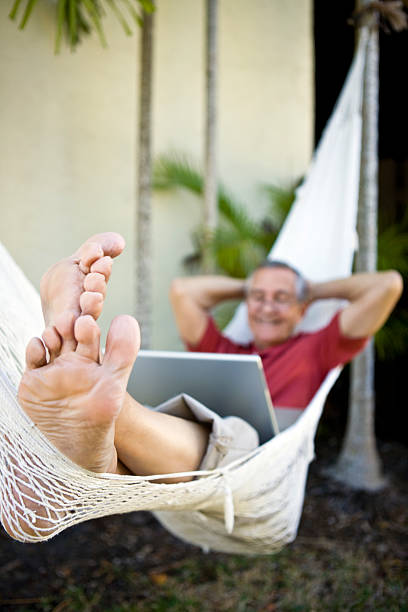 istock Senior man laying on hammock with laptop focus on feet 182852017