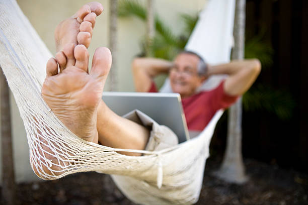 istock Senior man sitting on hammock with laptop hands behind head 182852022