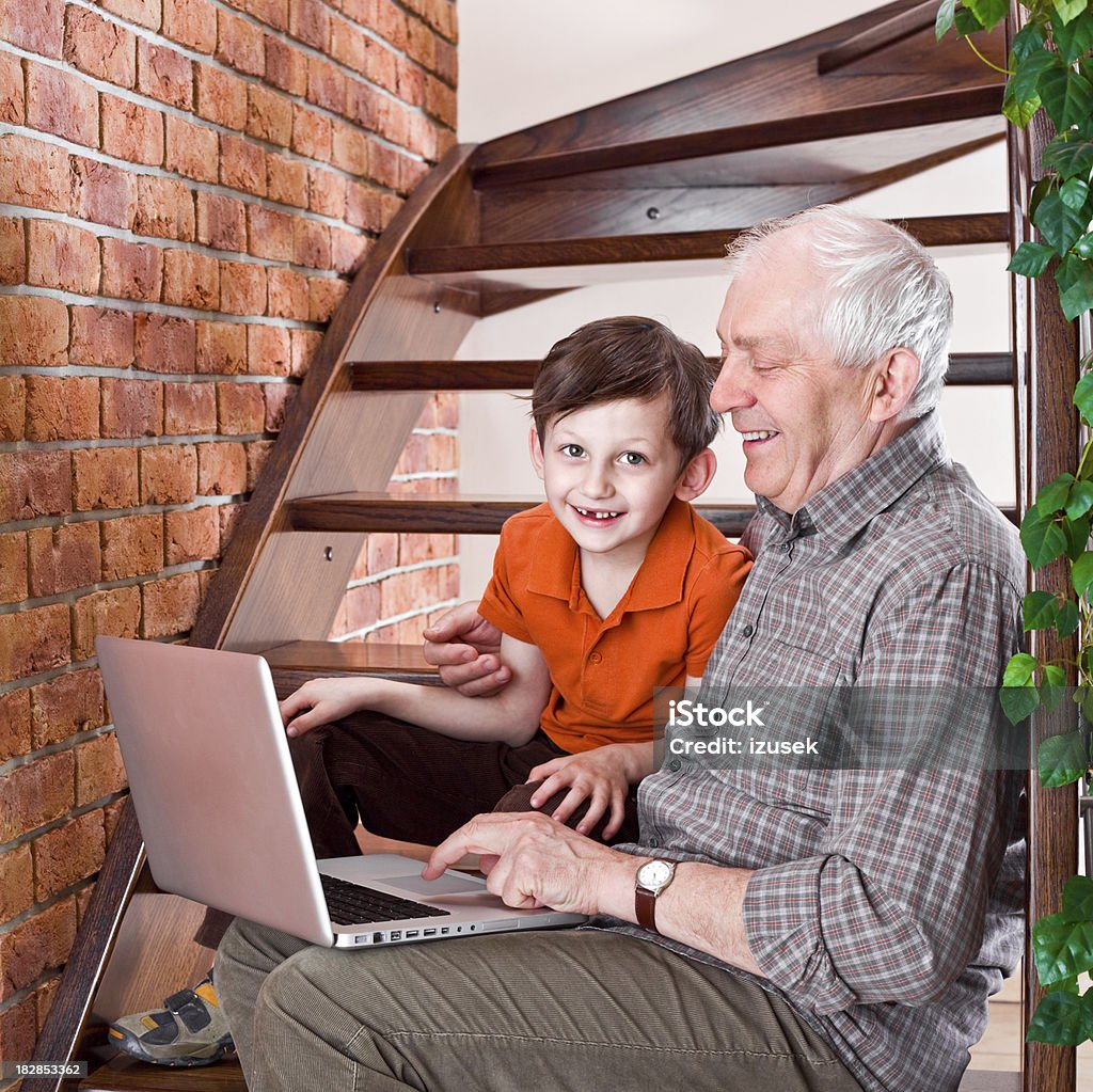 Nonno con nipote godendo di portatile - Foto stock royalty-free di Arancione