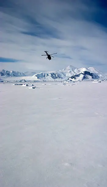 A Lynx helicopter flies over sea ice on the Antarctic Peninsula