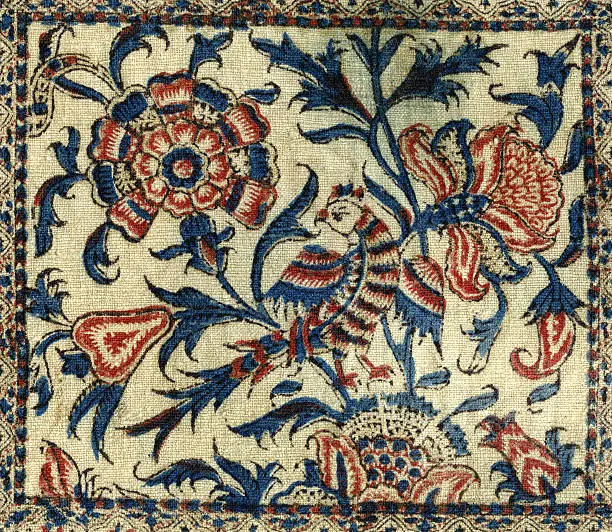 "Detail of an aged tapestry with stylized flowers, pear and bird."