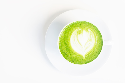 a glass of hot matcha green tea latte on white table.