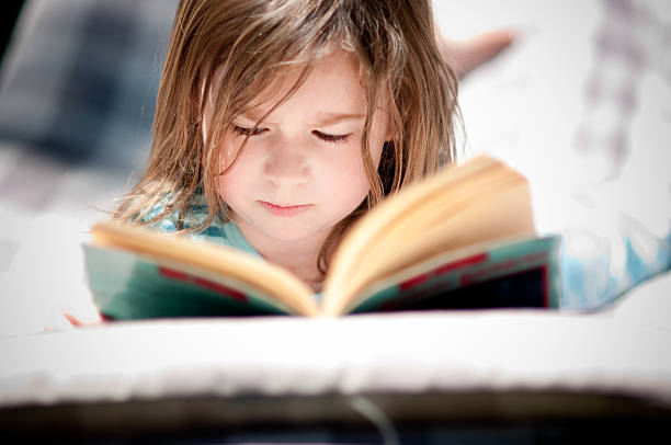 Color photo of a little girl lying on a hammock and reading a book.