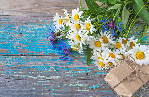 Bouquet of white daisies and bluecorns and handmade gift box on the old blue paint wooden background; space for text