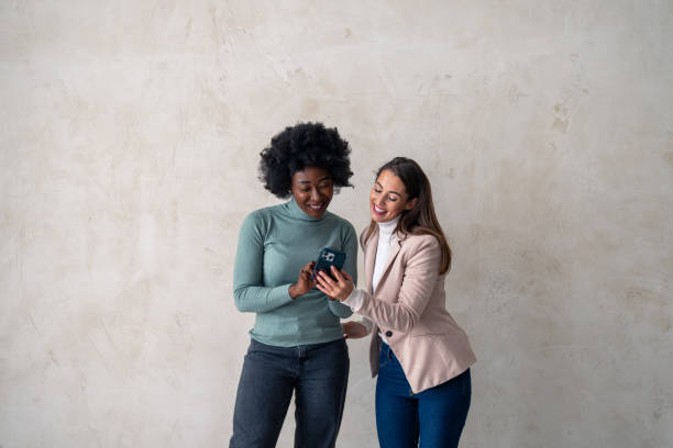 istock Two charming women standing against a studio background and looking at mobile phone 1828552073