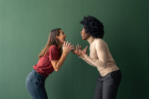 istock Two young interracial women yelling at each other against a green background in a studio 1828557326