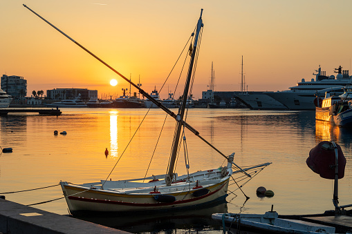 Old latin-rig fisherman boat in El Serrallo port of Tarragona with rising sun in background