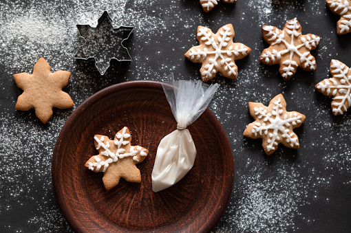 Making traditional Christmas ginger cookie. Star shape gingerbread cookie on black table background with flour and on plate, piping bag with sugar icing. Gingersnap cookie decoration, Selective focus.