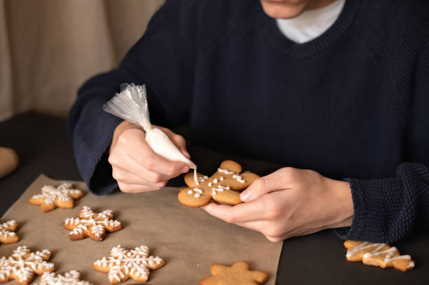 istock Boy in dark sweater decorating gingerbread man cookie with sugar icing, holding in hands piping bag and cookie. Christmas holiday celebration at home 1828569854