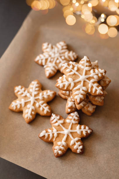 istock Star shape gingerbread cookie decorated with sugar icing on table, on brown baking paper background, with blurred garland lights. Holiday Christmas dessert, lifestyle, soft selective focus 1828571415