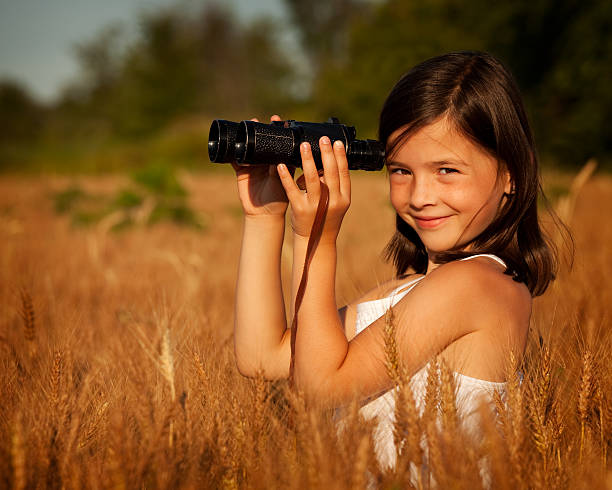 istock Cute young girl in field of ripe grain using binoculars 182857437