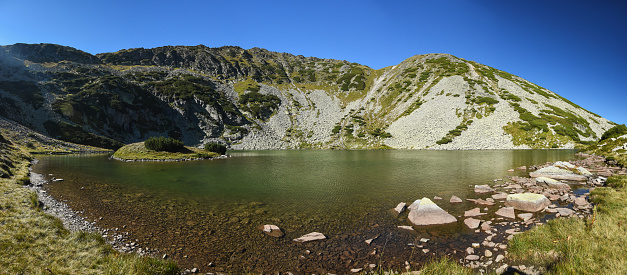 Panorama of Tau Tapului Glacier. The lake stands under the high crests of Retezat Mountains, in an alpine cauldron populated by mountain pines. Carpathian Mountains, Romania.