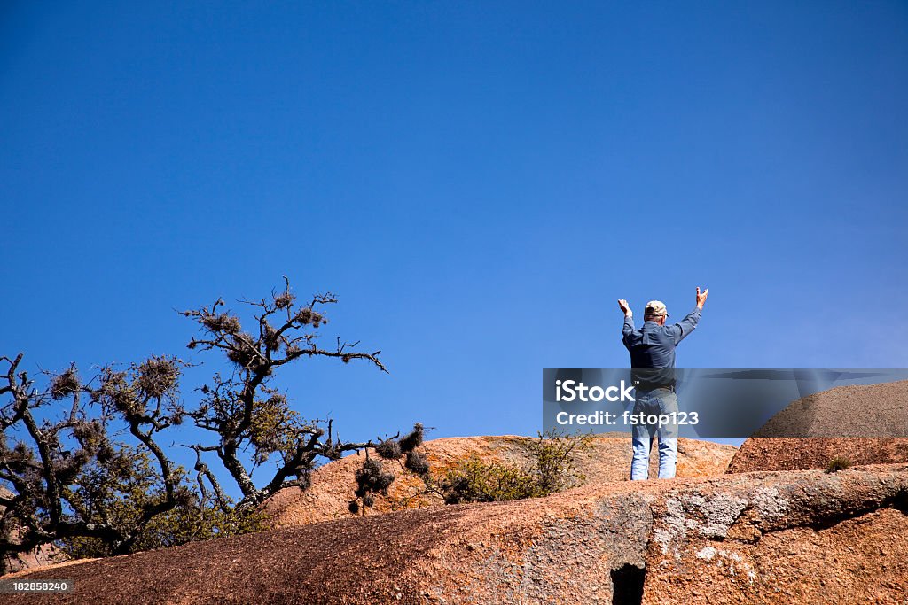 Man on high rocks with hands raised to the heavens. Adult Stock Photo