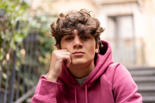 Young man in a pink hoodie looks contemplative against an urban backdrop, embodying a casual yet thoughtful demeanorx1z\