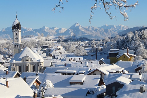 View of snow-covered Nesselwang with the parish church of St. Andreas and the Alps in the background. Nesselwang is also a vacation resort with winter sports. You can ski on the Alpspitze. Allgäu, Bavaria.