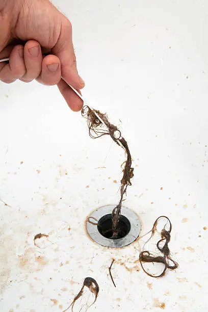 Wet hair being pulled from a drain with a plastic tool