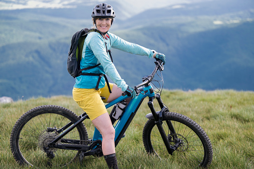 Portrait of adult female on electric mountain bike on green meadow. Healthy lifestyle concept.