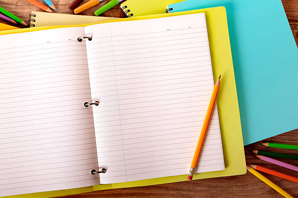 Student's desk with yellow project folder "Student's desk with yellow project folder surrounded by various pens, pencils and notebooks." homework books stock pictures, royalty-free photos & images