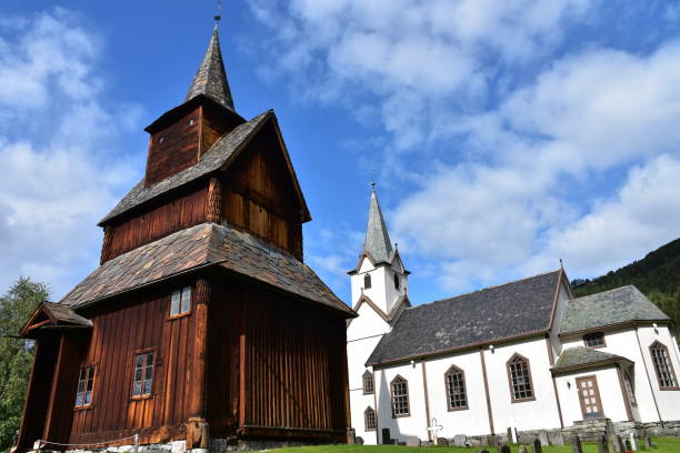 dos iglesias cercanas, una de madera marrón y otra de piedra blanca, en noruega - lom church stavkirke norway fotografías e imágenes de stock