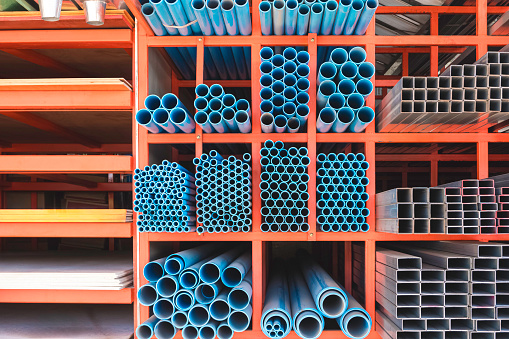 Various sizes of many blue PVC water pipes with rectangular carbon steel tubes and gypsum boards on storage shelf of building supply store
