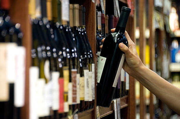 Choosing a Bottle of Wine A woman's hand reaches out to select a bottle of red wine from the shelf of a wine shop alcohol shop stock pictures, royalty-free photos & images