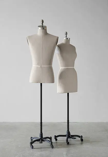 Two Mannequins photographed in a still life setting against a grey wall.