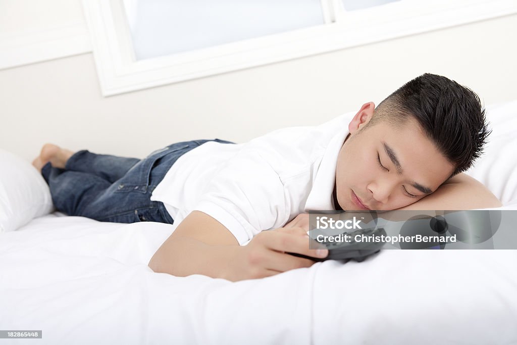 Uomo asiatico tenendo remote letto in camera da letto - Foto stock royalty-free di 20-24 anni
