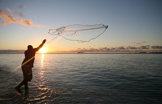 A man throws a fishing net during sunset in Fiji