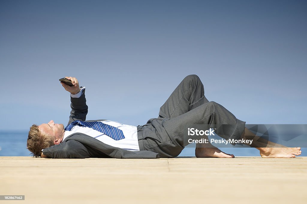 Pieds nus Homme d'affaires allongé de détente ensoleillée Dock avec téléphone - Photo de Costume habillé libre de droits