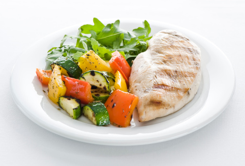 Grilled chicken and vegetables with arugula salad on a white background