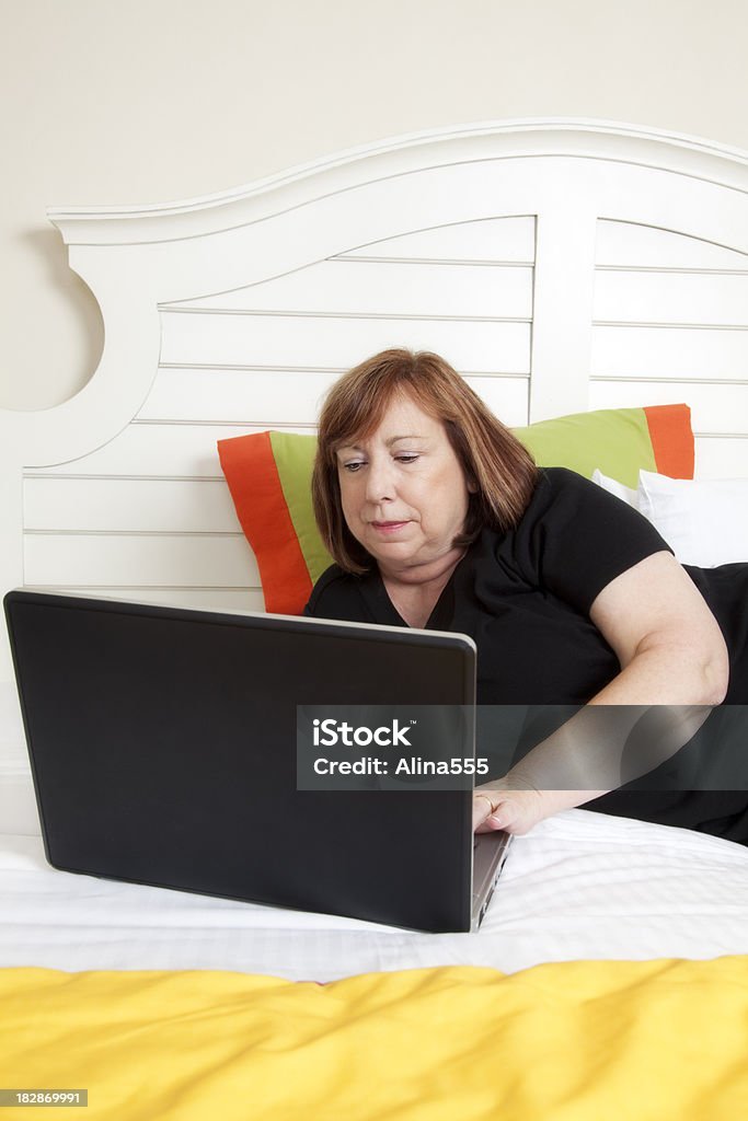 Femme âgée travaillant sur ordinateur portable et mettez-vous dans la chambre - Photo de 60-64 ans libre de droits